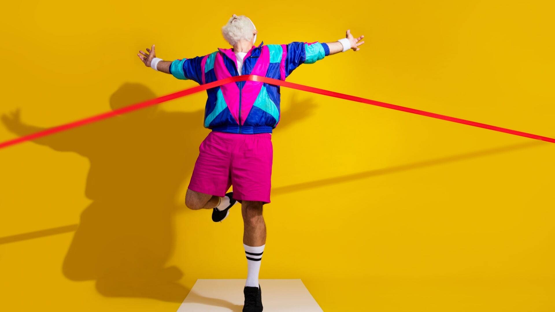 A person in vibrant retro athletic attire energetically crosses a red finish line against a bright yellow background, symbolizing success and achievement. This playful imagery conveys the concept of overcoming challenges and reaching goals, much like streamlining the SaaS sales cycle for optimal performance.