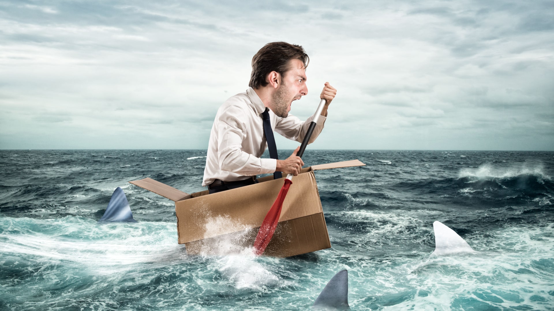 man in a cardboard box in the ocean paddling